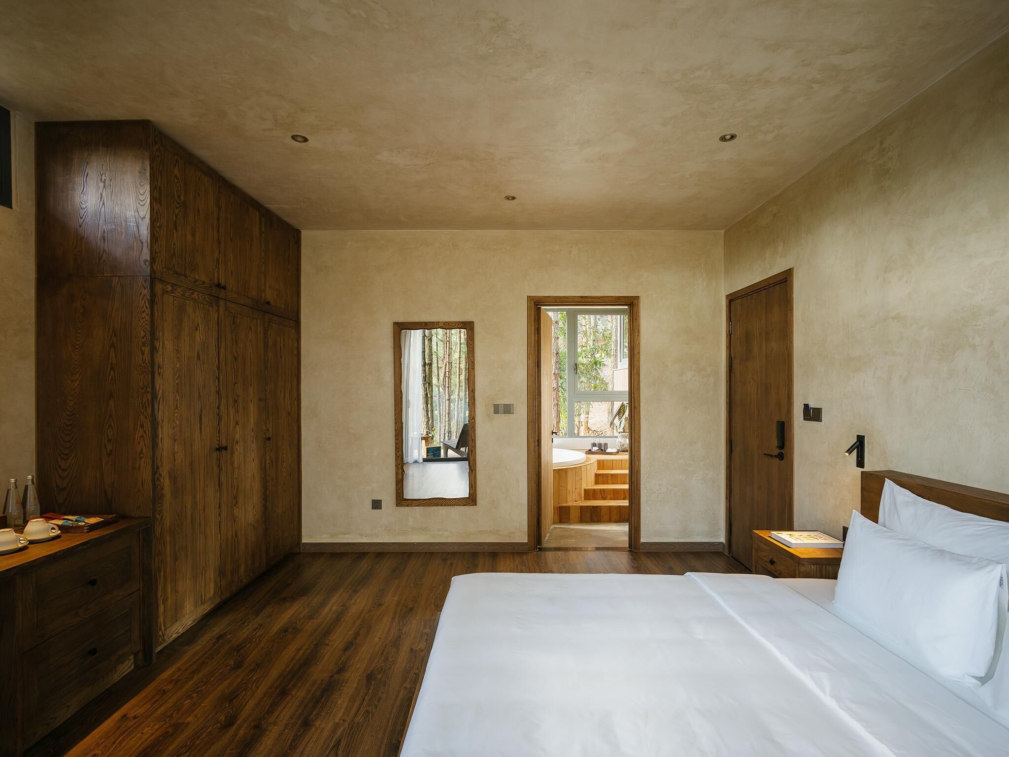 Une chambre avec un grand lit, une armoire en bois et une vue sur la salle de bain par une porte ouverte.