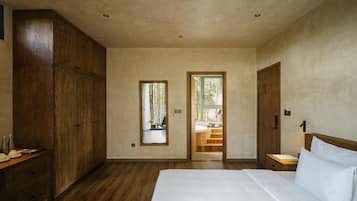 Une chambre avec un grand lit, une armoire en bois et une vue sur la salle de bain par une porte ouverte.