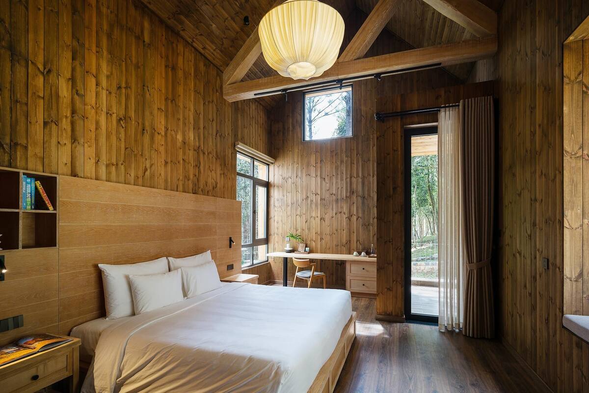 A wooden room with a large bed, a desk, and a window.