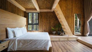 A bedroom with a wooden ceiling, a large bed, a window with a view of trees, and a small seating area with plants. - Mơ Stay Forest Resort (Xuan Huong - Da Lat)