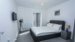A modern bedroom with a large bed, bedside tables, a TV, and a radiator. - Captivating 1-bed Apartment in London (London)