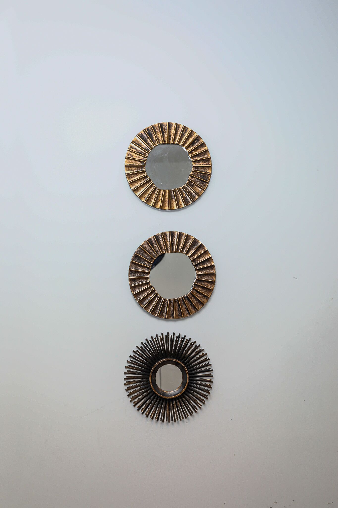 Trois miroirs muraux décorés d’un motif en forme de soleil rayonnant.