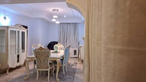Un comedor con una mesa blanca, sillas ornamentadas, un armario y una araña.