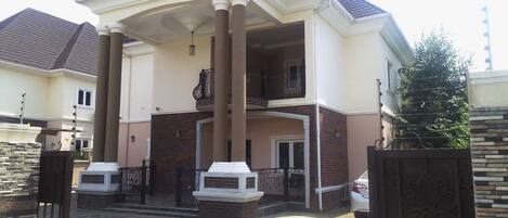 A two-story house with a central balcony, a covered entrance, and a paved driveway.