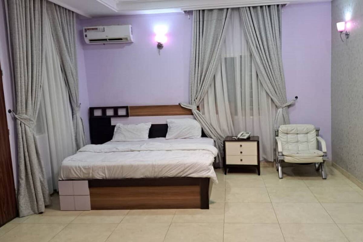 Quarto com cama, mesas de cabeceira, uma cadeira, ar condicionado e cortinas.