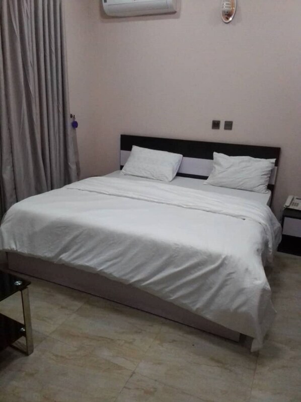A neatly made bed with white bedding in a room with a tiled floor and a wall-mounted air conditioner.