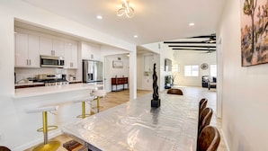 Una cocina moderna con armarios blancos, electrodomésticos de acero inoxidable y una zona de comedor con una mesa larga y sillas.