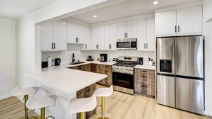 Una cocina moderna con armarios blancos, electrodomésticos de acero inoxidable y una isla central con taburetes de bar.