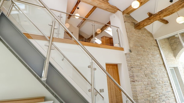 Un escalier avec des rampes en verre, des poutres en bois et un mur en briques.