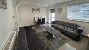 A modern living room with a sectional sofa, a glass coffee table, and a dining area with chairs.