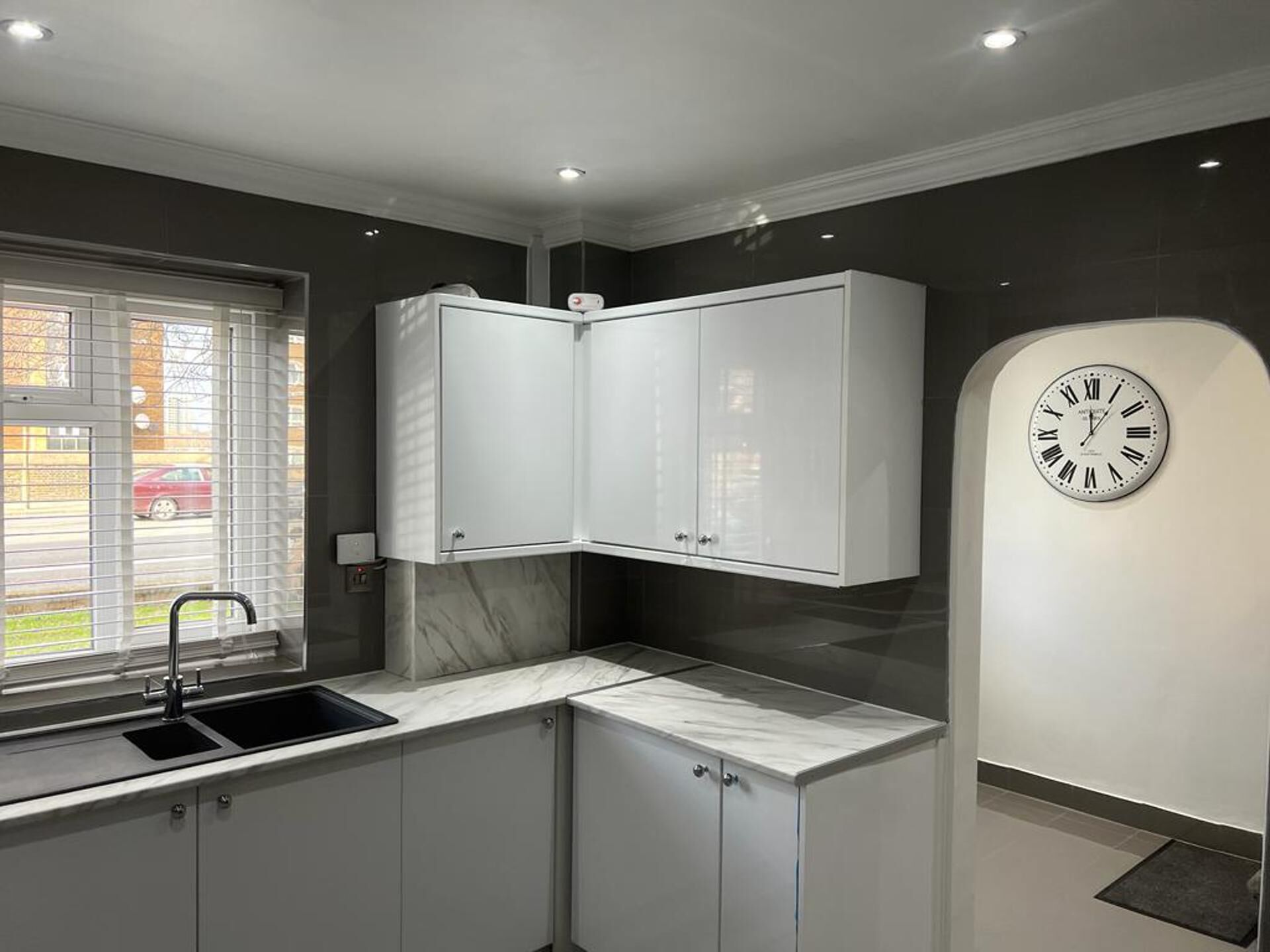 Une cuisine moderne avec des meubles blancs, un plan de travail en marbre, un évier et une horloge murale.