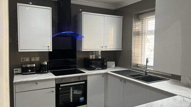 A modern kitchen with white cabinets, a black range hood, a built-in oven, and a sink.
