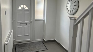 A hallway with a white door, a clock on the wall, and a staircase.