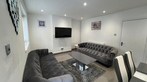 A modern living room with a grey sectional sofa, a coffee table, and a TV mounted on the wall.