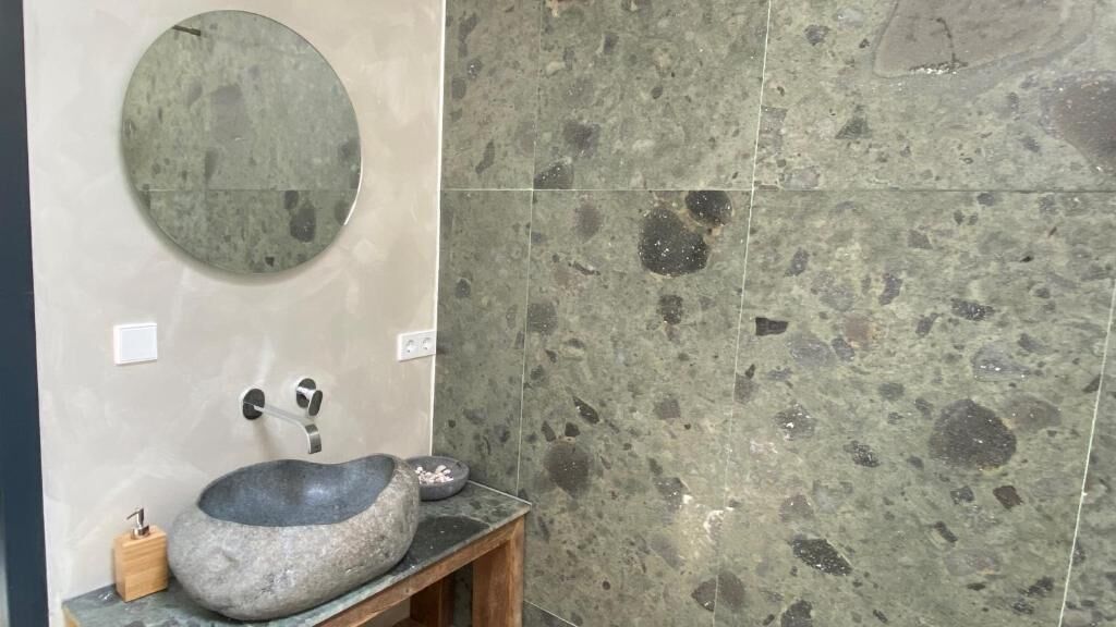 A bathroom with a stone sink, a round mirror, and a tiled wall.