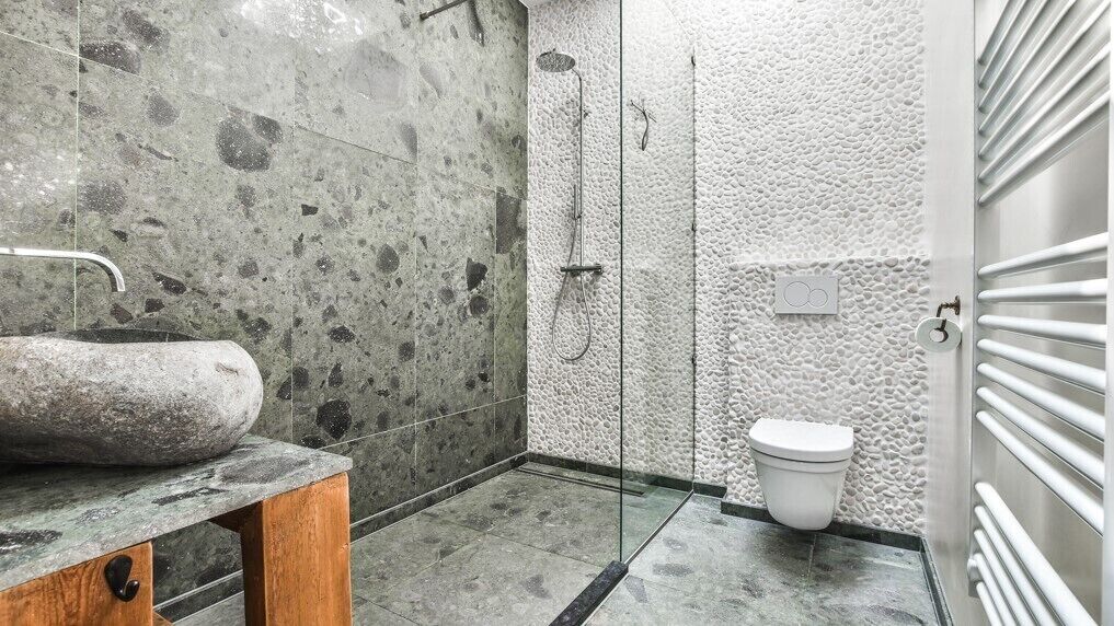 Een badkamer met een stenen wasbak, een douche met glazen wanden en een wit toilet.