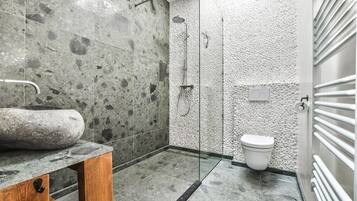 Een badkamer met een stenen wasbak, een douche met glazen wanden en een wit toilet.