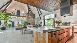 A spacious kitchen with a large island, wooden cabinets, and a stone accent wall. - het Lichthuis (Zandvoort)