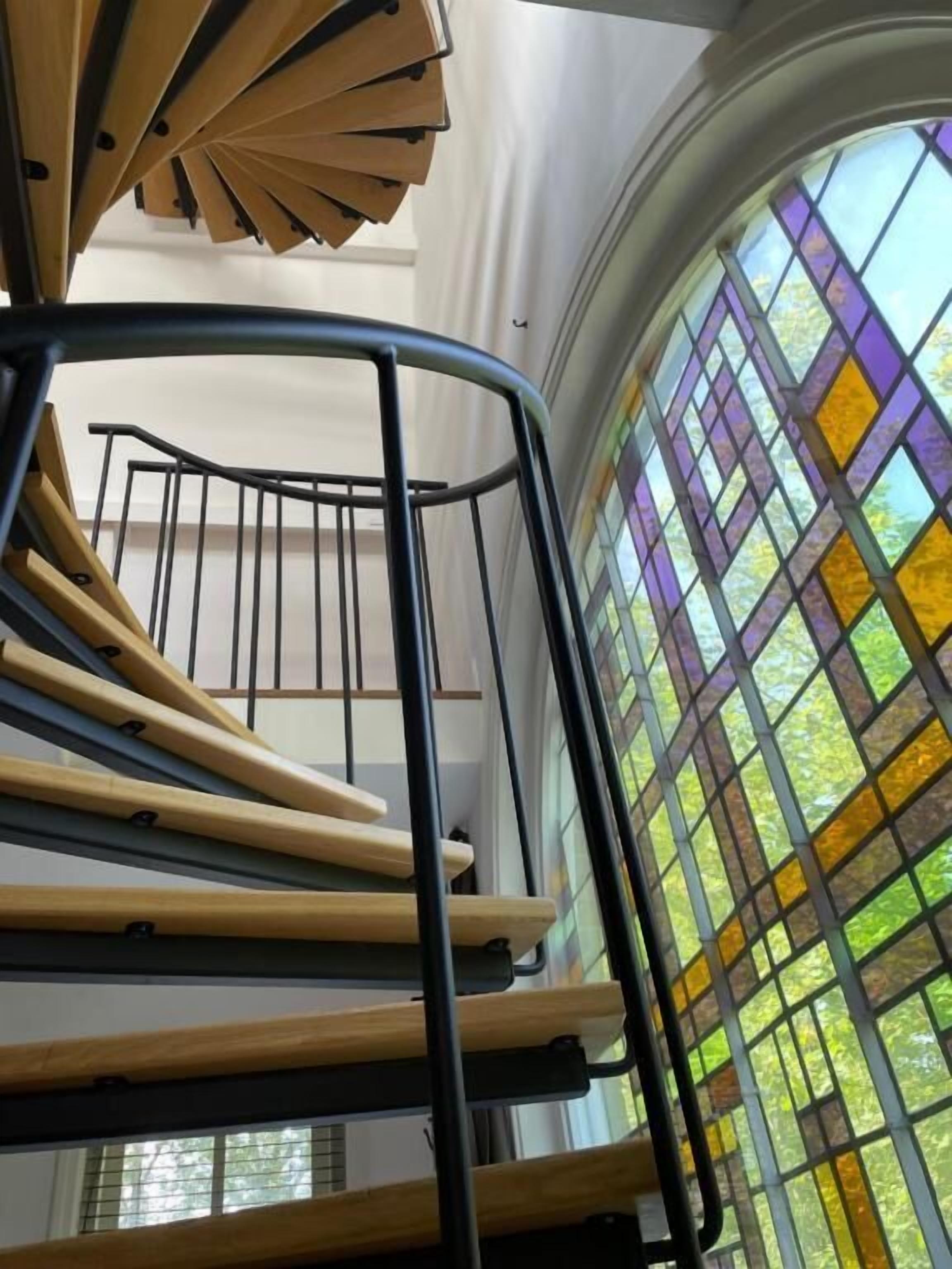 Un lit superposé avec une barrière métallique et, en arrière-plan, un vitrail.