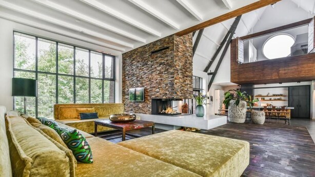 A spacious living area with a stone fireplace, large windows, and a high ceiling. - het Lichthuis (Zandvoort)