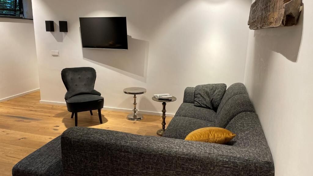 Een moderne woonkamer met een grijze bank, een zwarte fauteuil en een kleine ronde tafel.