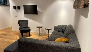 Een moderne woonkamer met een grijze bank, een zwarte fauteuil en een kleine ronde tafel.