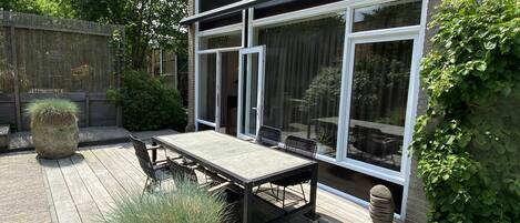Un patio con una mesa y sillas, un amplio ventanal corredero y una terraza de madera.