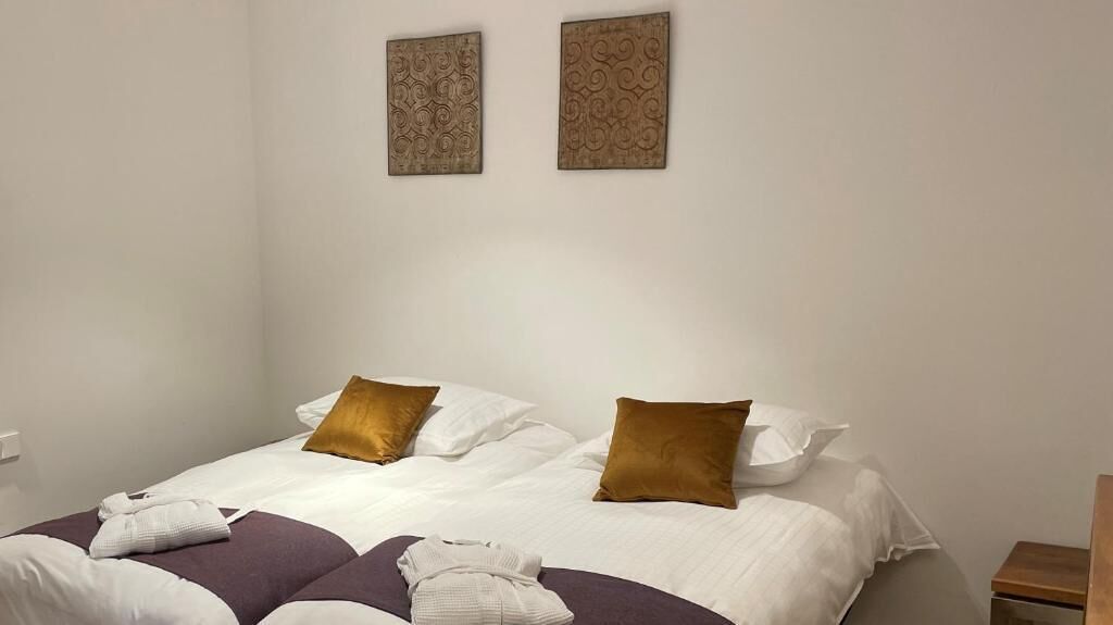 A neatly made bed with white and brown bedding, two decorative wall pieces, and a wooden nightstand.