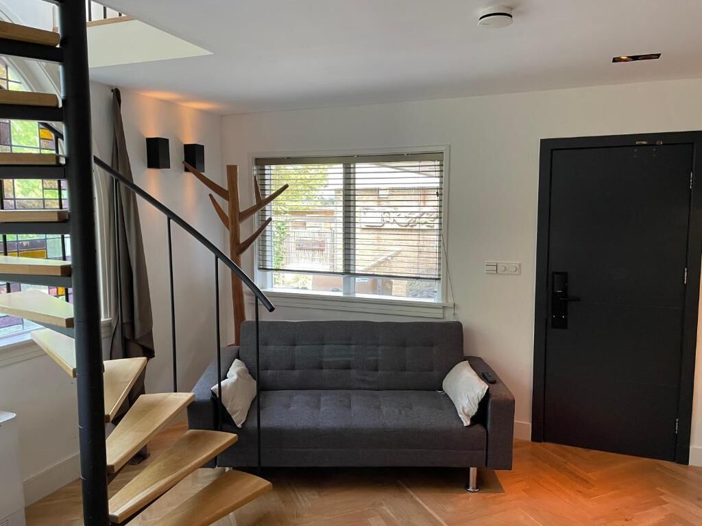 Un interior moderno con un sofá gris, una escalera de madera y una puerta negra.