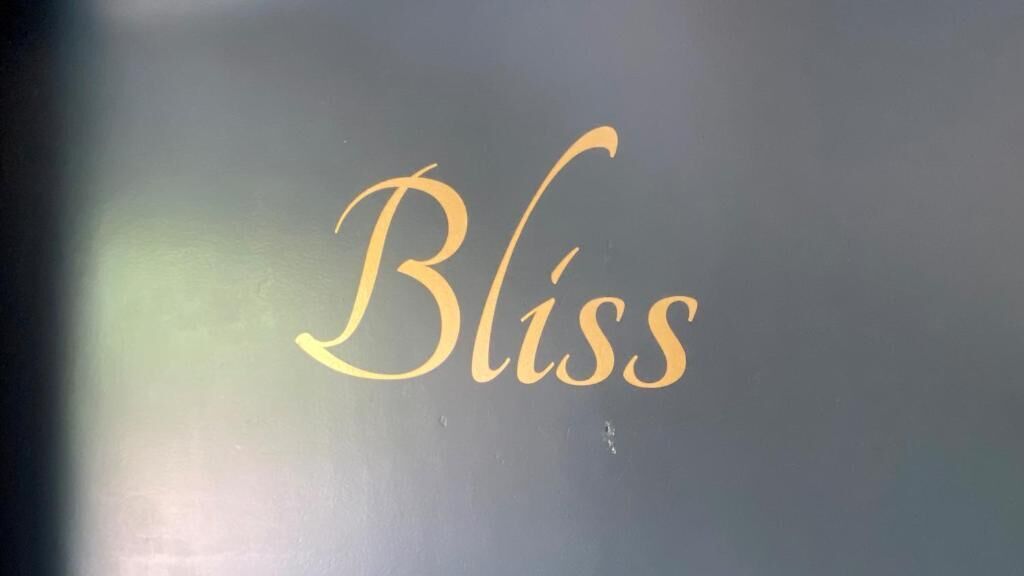 Ordet "Bliss" i flydende, gylden skrift mod en mørk baggrund.
