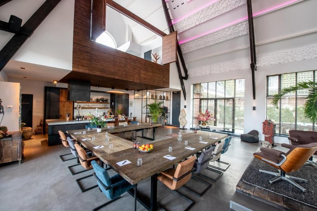 A spacious dining area with a long wooden table, multiple chairs, and a kitchen in the background.