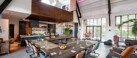 A spacious dining area with a long wooden table, multiple chairs, and a kitchen in the background.