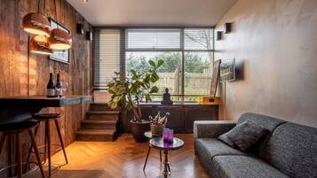 Un salon moderne avec un mur en bois, un canapé gris, une table basse ronde et un coin bar avec des tabourets.