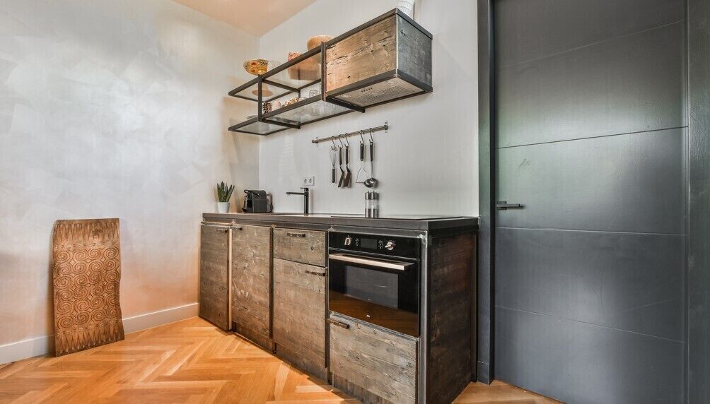 A compact kitchen with wooden cabinets, a built-in oven, and a hanging utensil rack.