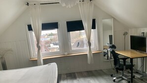 A bedroom with a bed, a desk, a chair, a TV, and a window with curtains. - Charming Apartmemt in Stockholm City (Stockholm)