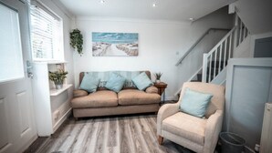 Ein Wohnzimmer mit einem beigen Sofa, einem hellblauen Sessel und einem Landschaftsbild an der Wand.