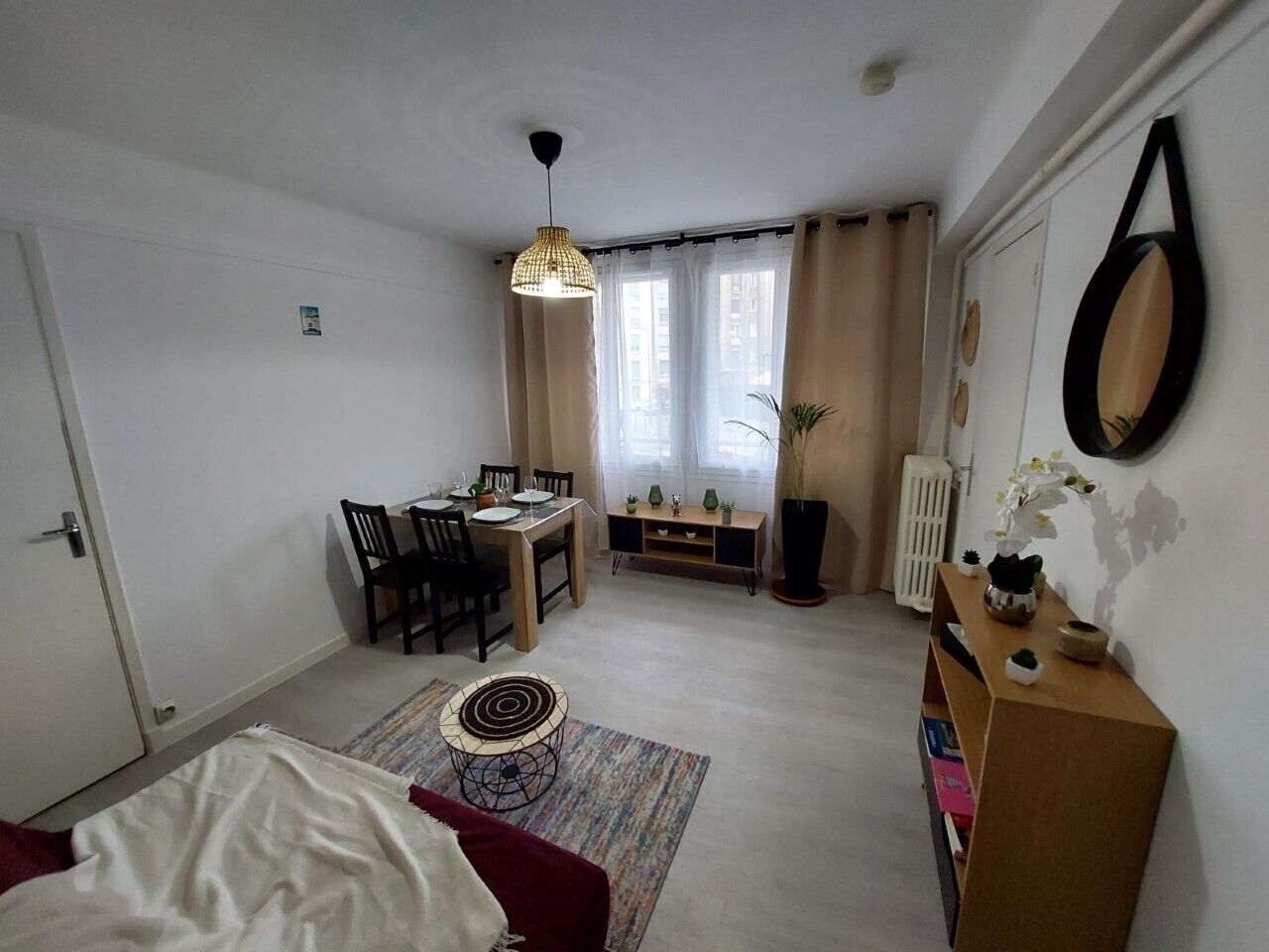 Quarto compacto com cama, mesa de jantar com cadeiras, pequena área de cozinha e radiador.