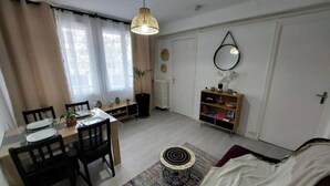 Ett kompakt vardagsrum med en matplats, ett litet runt bord, en soffa, en hängande lampa, en bokhylla och ett element.