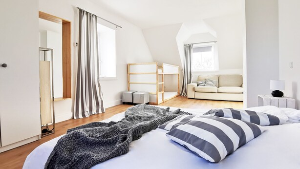 Een moderne slaapkamer met een groot bed, een sofa, een houten garderobe en een spiegel.