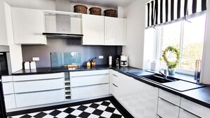 Een moderne keuken met witte kasten, een zwart-wit geruite vloer, een inbouwfornuis en een raam met uitzicht op bomen.