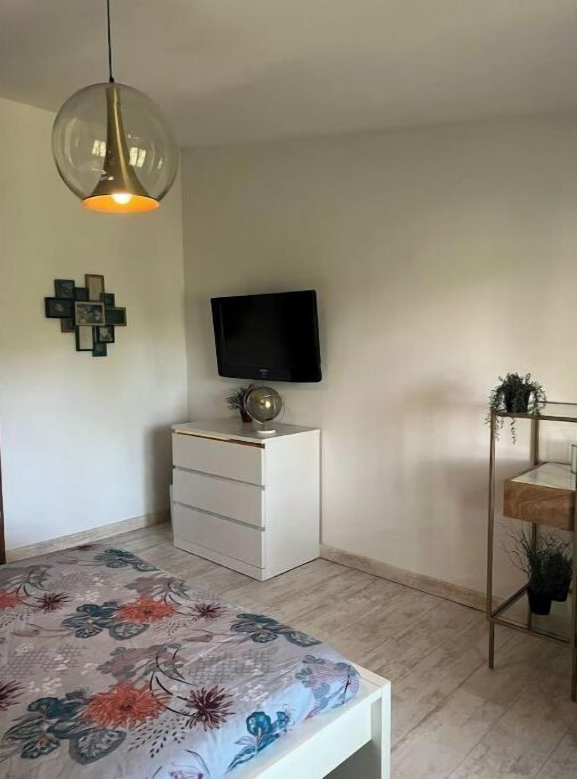 Une chambre à coucher comprenant un lit, un téléviseur, une commode et un luminaire suspendu.