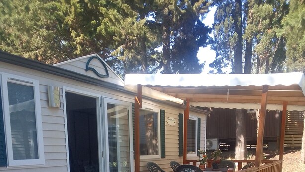 Eine Holzterrasse mit überdachter Sitzgruppe, ein kleines Gebäude mit Schiebetür und ein Holzzaun.
