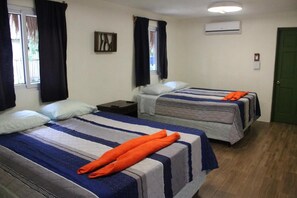 Una habitación con dos camas, cada una con cubrecama a rayas, una mesita de noche y una ventana con cortinas.