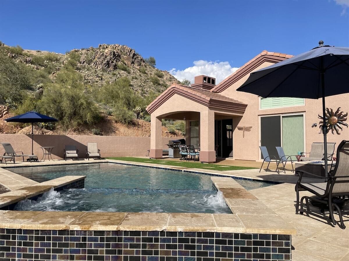 A swimming pool with a hot tub, surrounded by lounge chairs and a patio table.