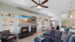 A spacious living room with a fireplace, a ceiling fan, and a dining area in the background.