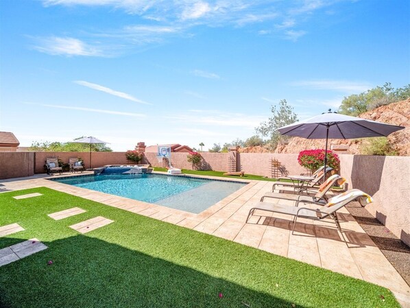A backyard with a swimming pool, lounge chairs, and a patio area.
