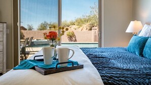 A bedroom with a bed, a tray with two white mugs, and a vase with flowers.
