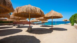 Une plage avec des parasols en chaume et un ciel bleu azur.