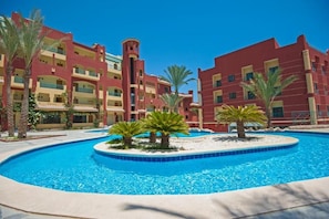 Ein Hotel mit Swimmingpool, umgeben von Palmen und einer roten Fassade.