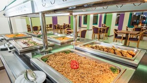 Un buffet proposant une variété de plats, notamment du riz, des légumes et des plats de viande, dans un espace de restauration bien éclairé, équipé de tables et de chaises.
